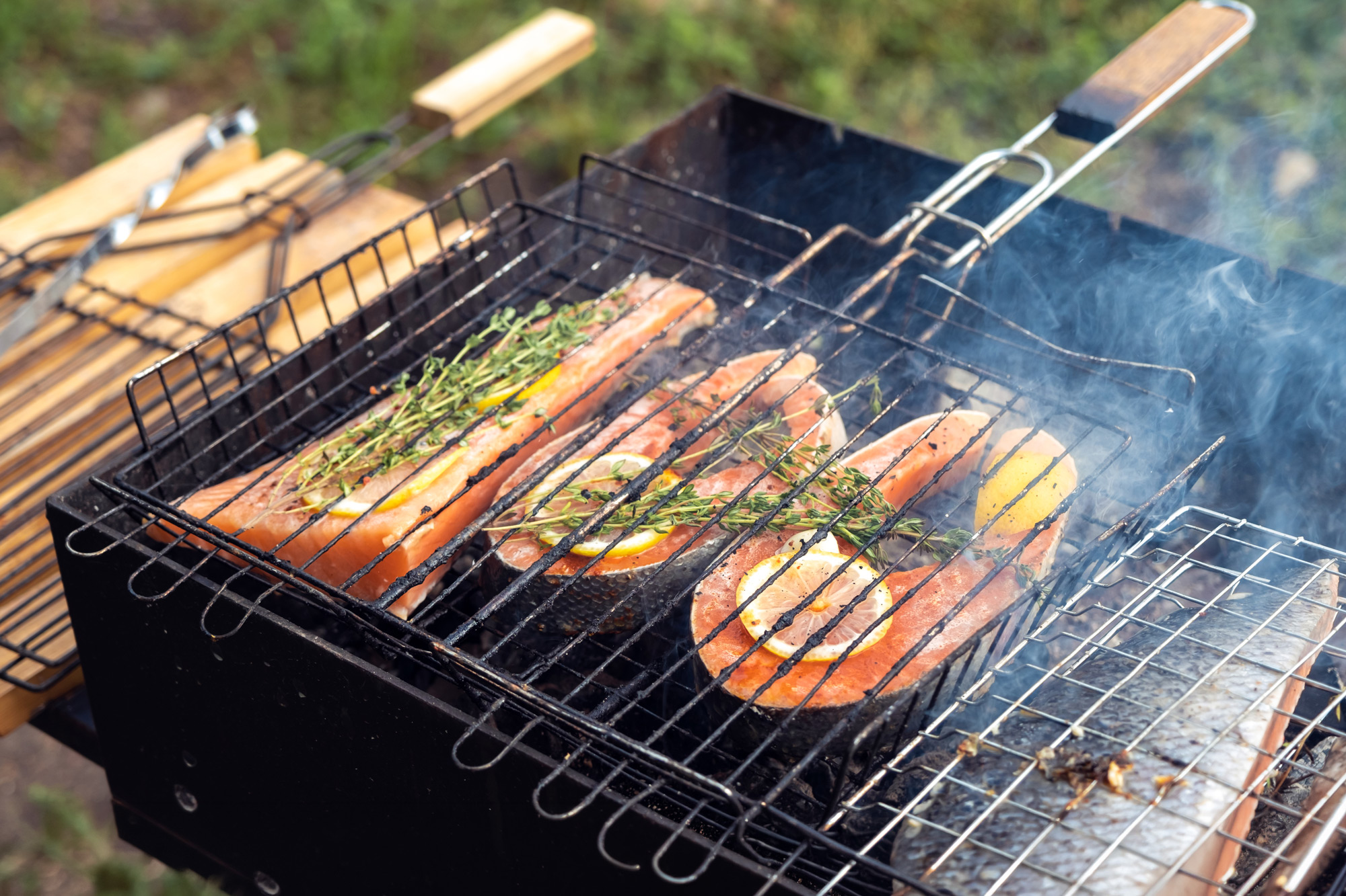 Saftiga laxbiffar ligger i en grillkorg på en utegrill och tillagas utomhus under sommaren.